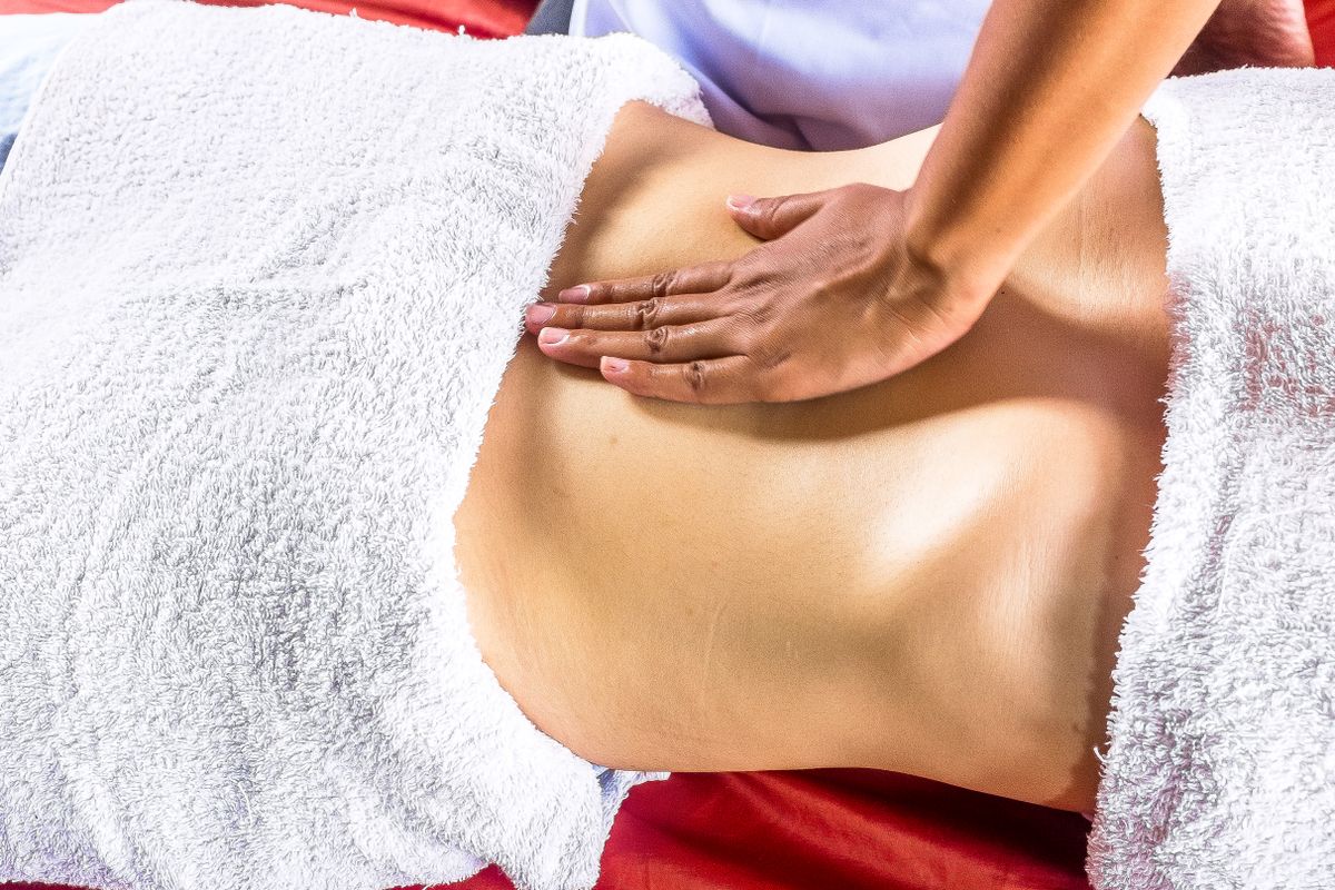 Therapist's hand massaging a client's lower back, draped with towels