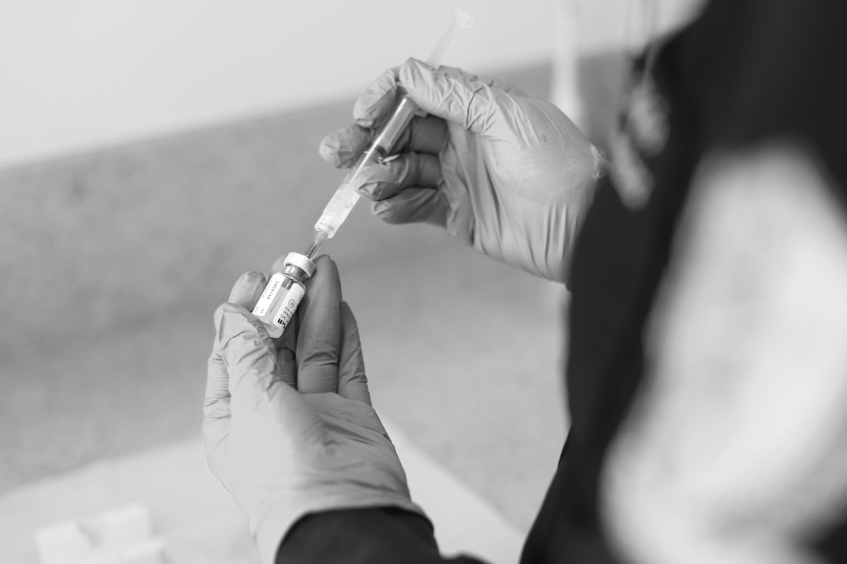 Gloved hands drawing medicine from a vial into a syringe