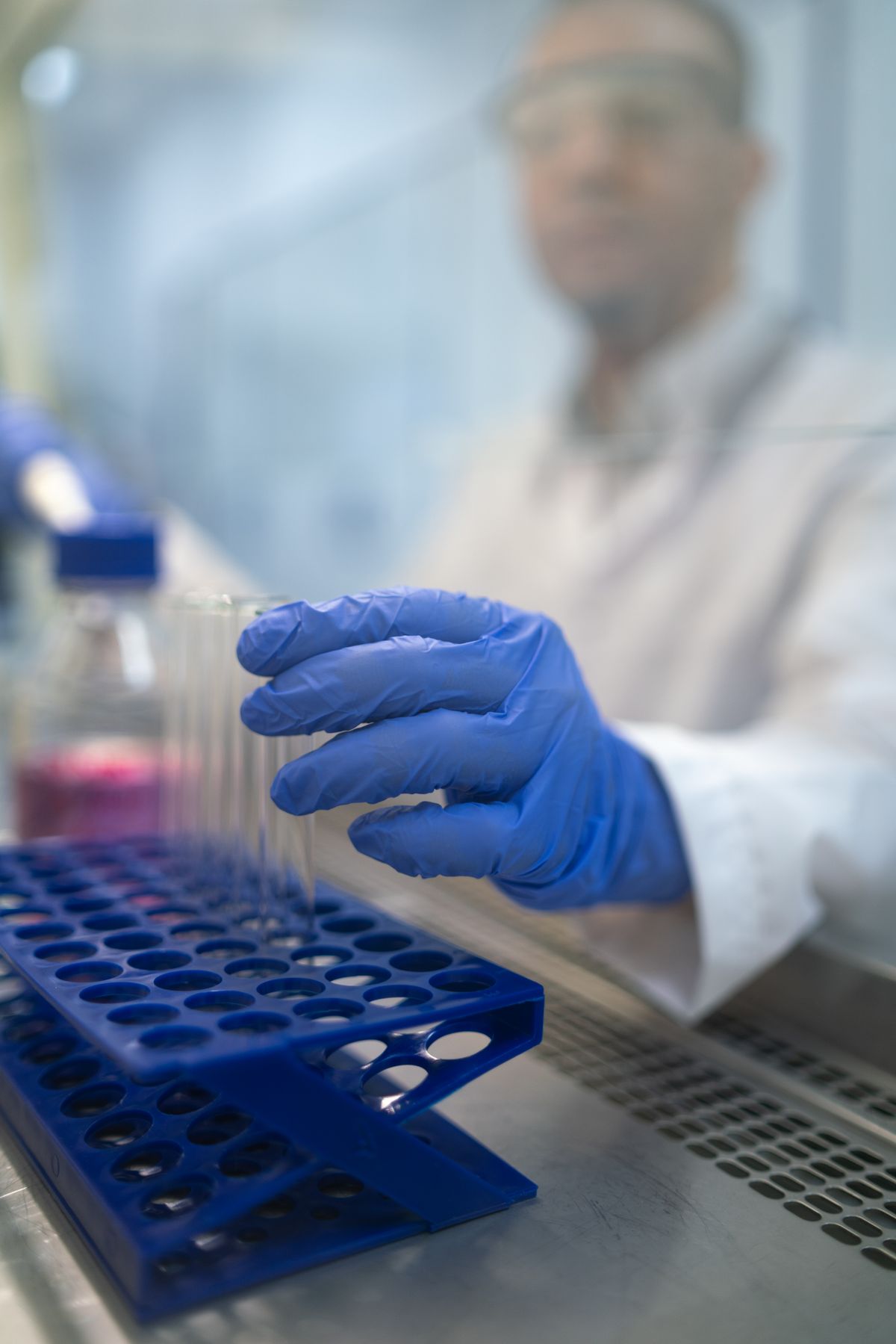 Lab worker reaching for test tubes in a rack behind glass