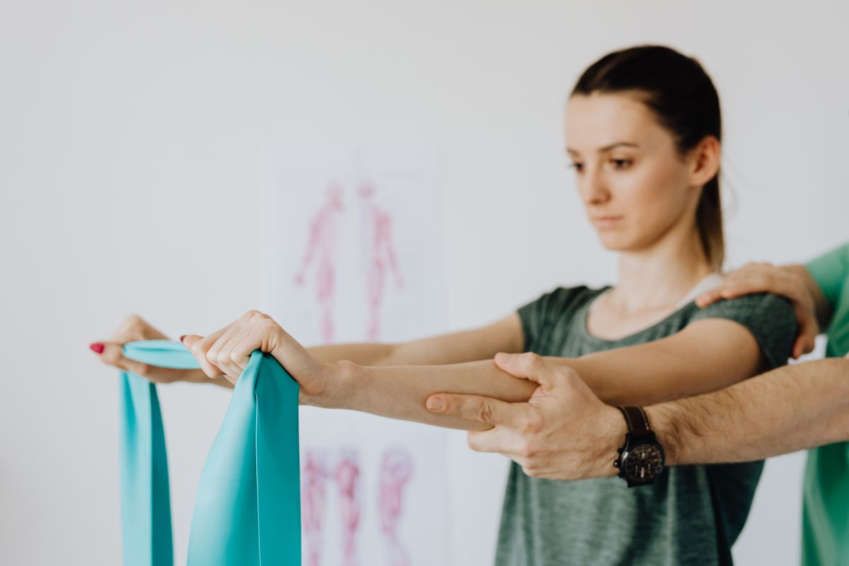 Therapist guiding a patient through a resistance-band stretch next to a posture chart