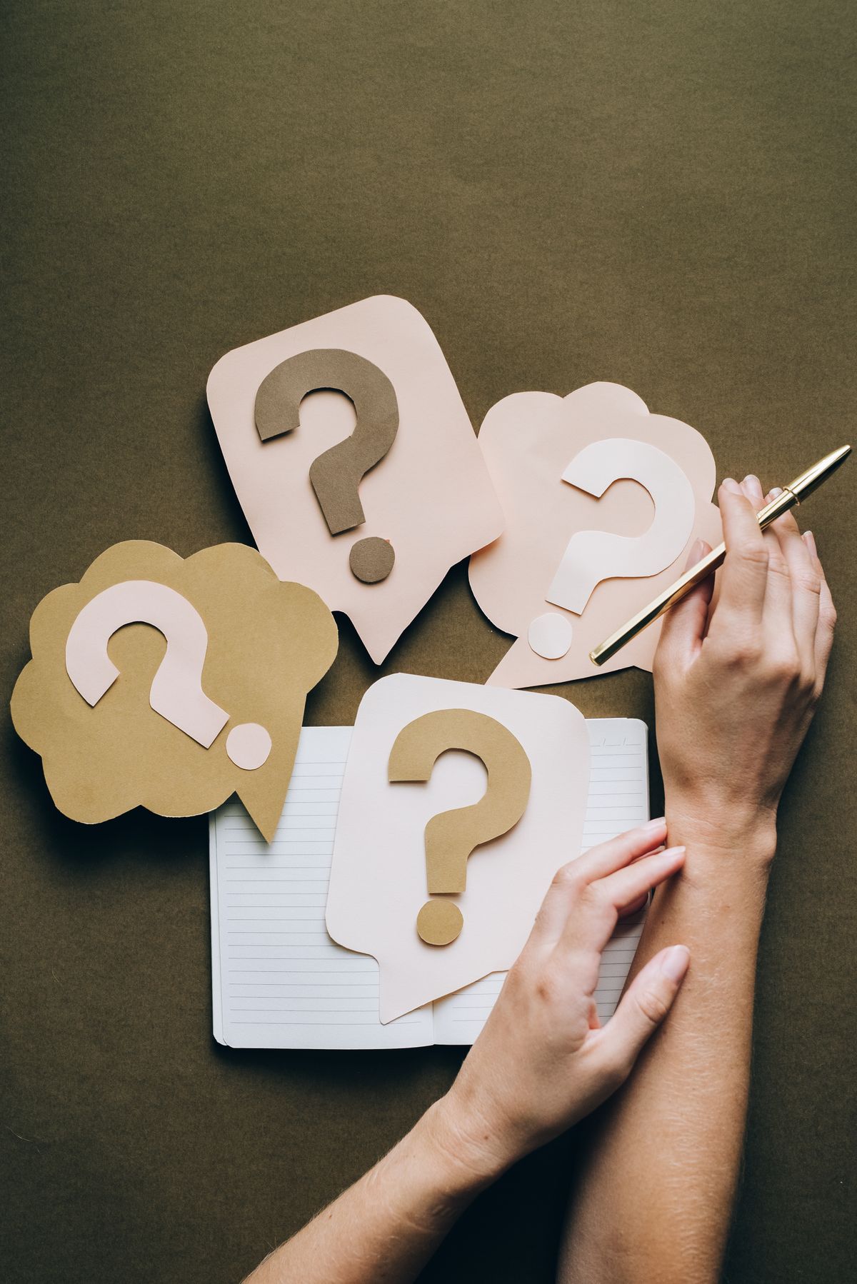 Hands holding a pen beside paper question-mark cutouts on a notebook