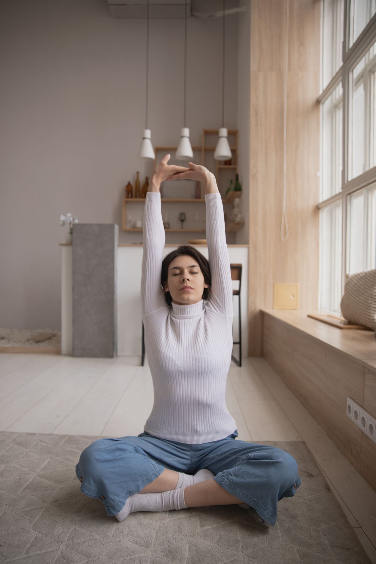 Woman sitting cross-legged, stretching her arms overhead